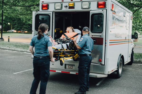 Paramédicos con uniforme azul subiendo a una paciente en una camilla a una ambulancia
