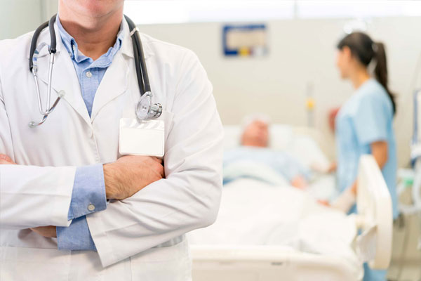 Doctor con bata blanca y camisa azul frente a un paciente en una camilla y una enfermera