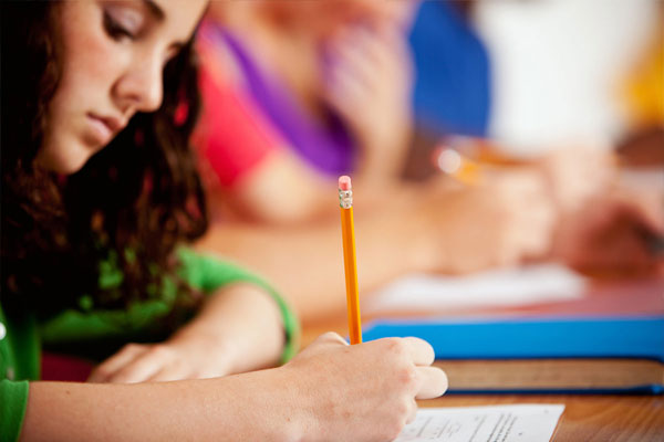 Niña sentada con un lápiz escribiendo en una hoja blanca