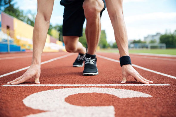 Hombre agachado con short y tenis negros preparado para correr